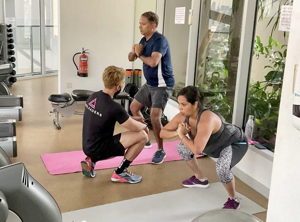 Personal trainer from Athleaders helping two buddies with workout in condo-gym